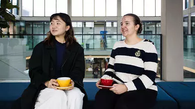 image of two students sat down on a bench facing the camera