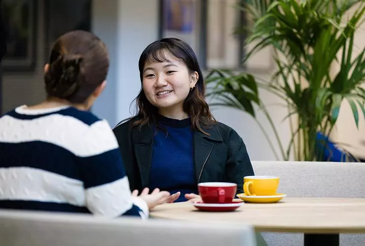 image of two female students sat at a table talking, one with her back to the camera